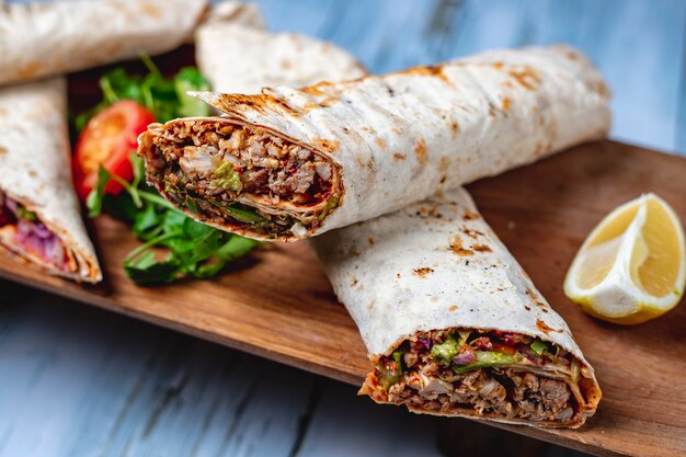 Seitenansicht Hühnerdoner mit grüner Gurke Tomatensauce Gurke rote Zwiebel in Pita und Zitronenscheibe auf einem Brett