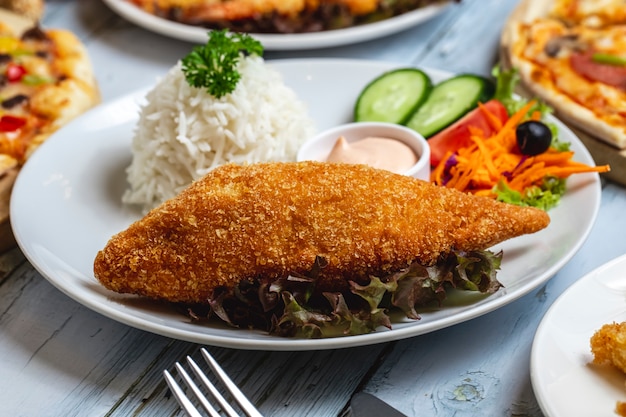 Seitenansicht Hühnerschnitzel knusprige Panco Hühnerbrust mit Reis garnieren Gurken Tomaten Karotte und Sauce auf einem Teller