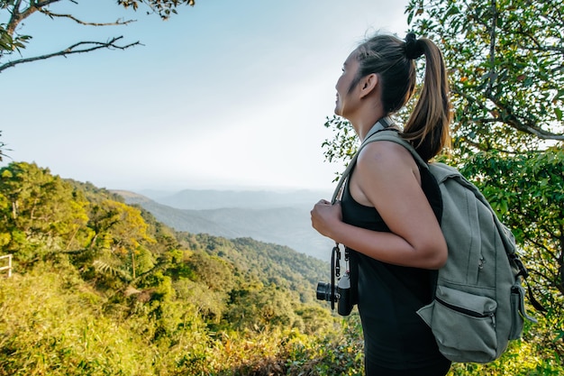 Seitenansicht Junge asiatische Wanderfrau, die am Aussichtspunkt steht und eine schöne Aussicht mit glücklichem Gipfel und Sonnenstrahl-Kopienraum hat