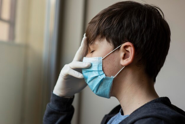 Seitenansicht Junge mit medizinischer Maske, die sein Gesicht berührt