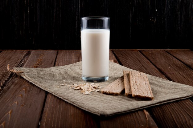 Seitenansicht Knuspriges Knäckebrot mit Haferflocken und Glas Milch auf Holztisch