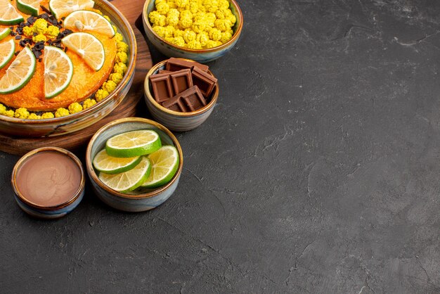 Seitenansicht Kuchen und Limetten Bonbons Schokoladencreme und geschnittene Limetten in Schalen neben dem appetitlichen Orangenkuchen auf dem Tisch