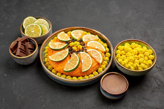 Seitenansicht Kuchen und Süßigkeiten appetitlicher Kuchen mit Zitrusfrüchten und Schalen mit Schokoladencreme gelbe Bonbons Schokolade und Limettenscheiben