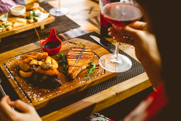 Seitenansicht Lachssteak mit Kartoffel in einer ländlichen Granatapfelsauce Salz und Glas Wein auf dem Tisch