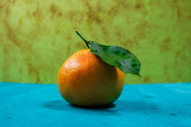 Seitenansicht Mandarine mit Blatt auf blau strukturiertem Tisch und grüner Textur. horizontal