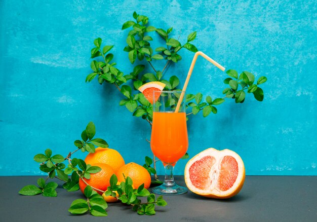 Seitenansicht Mandarinen mit Blättern, Orange und Saft auf blau strukturierter Oberfläche. horizontal