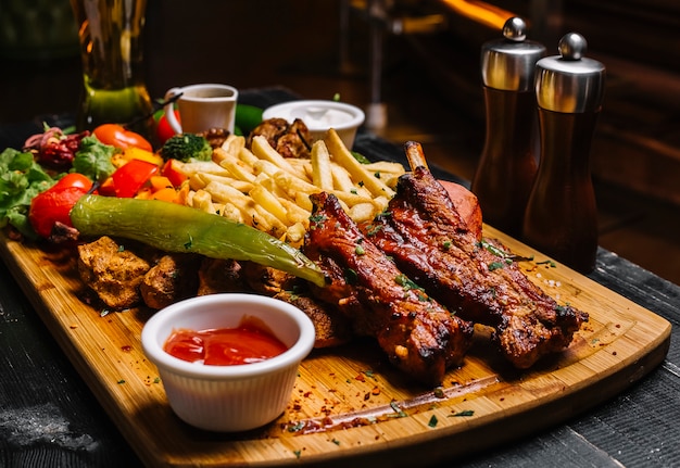 Seitenansicht mischung von fleischsnacks mit pommes frites gegrilltem gemüsesalat und saucen auf dem brett