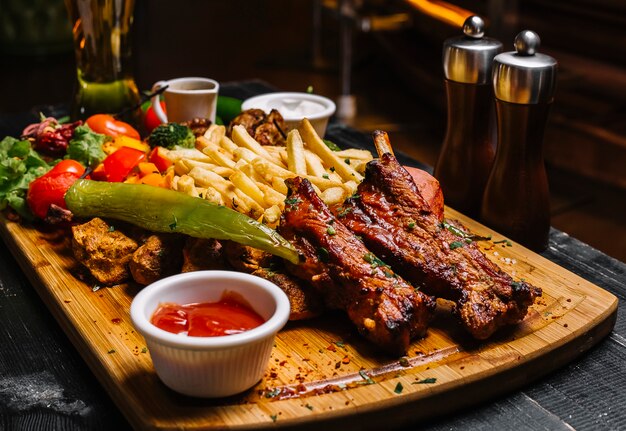 Seitenansicht Mischung von Fleischsnacks mit Pommes Frites gegrilltem Gemüsesalat und Saucen auf dem Brett