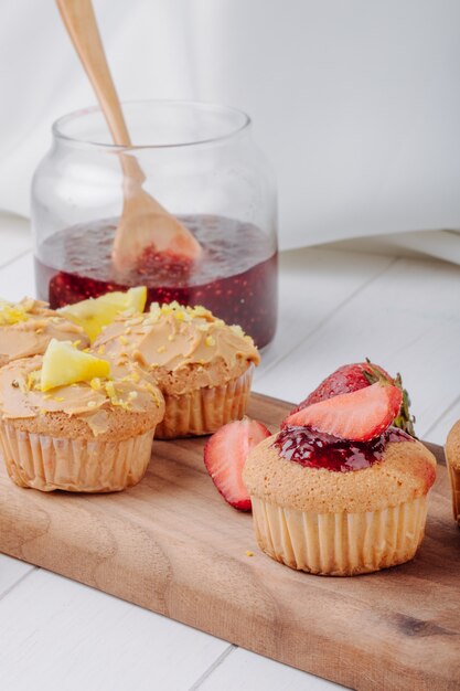 Seitenansicht Muffins mit Erdbeeren und Zitrone auf einem Brett mit einem Glas Marmelade