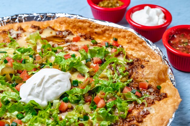 Seitenansicht Nachos gebratene Tortila mit Hackfleischkäse frische Tomatensalat Frühlingszwiebel saure Sahne und gehackter Jalapenopfeffer und Saucen auf dem Tisch