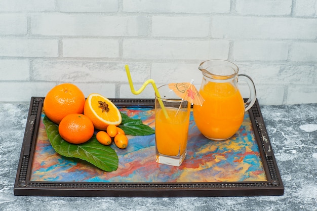 Seitenansicht Orangen im Rahmen mit abstrakten Farben mit Saft in Gläsern, Blättern, Mandarine auf heller Ziegelstrukturoberfläche. horizontal