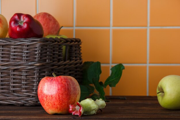 Seitenansicht Äpfel im Korb mit gebissenem auf hölzernem und orange Fliesenhintergrund. horizontal