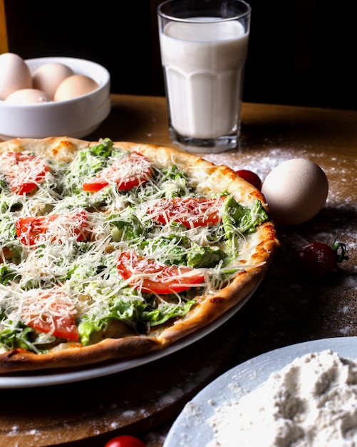 Seitenansicht Pizza mit Tomaten mit Eiern ein Glas Milch und Mehl auf dem Tisch