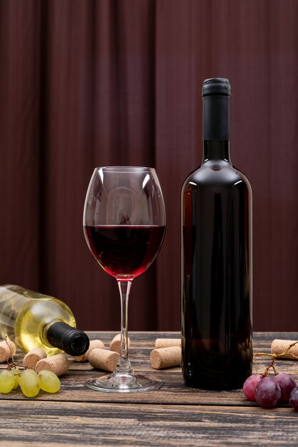 Seitenansicht Rotwein in Flasche, Glas und Traube auf dunklem Tisch und vertikal