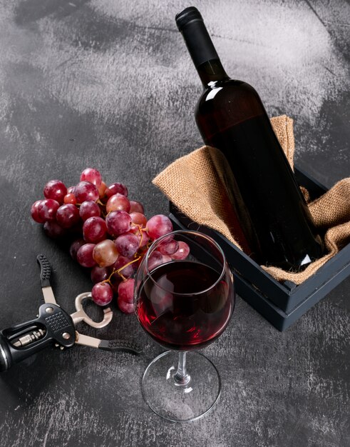 Seitenansicht Rotwein mit Traube in Kiste mit Sackleinen auf schwarzem Stein vertikal