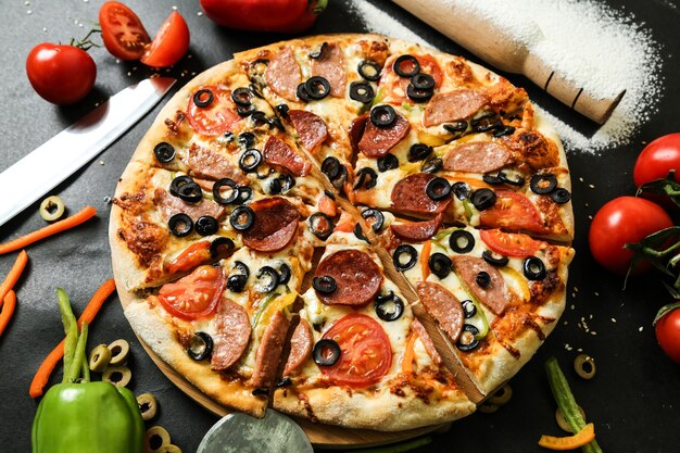 Seitenansicht Salami-Pizza mit Paprika-Tomaten-Oliven und Nudelholz mit Mehl
