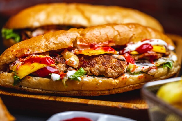 Seitenansicht Sandwich Weißbrot mit gegrilltem Fleisch Schnitzel Käse Salat Pommes Frites Mayo und Ketchup auf einem Boardjpg