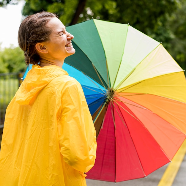 Seitenansicht-Smiley-Frau, die einen bunten Regenschirm hält