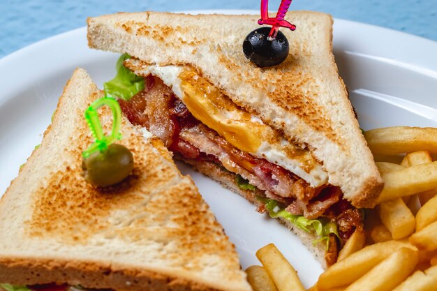 Seitenansicht Specksandwich mit gebratenem Speck Salatbrot Toast schwarze und grüne Oliven Pommes Frites auf einem Teller