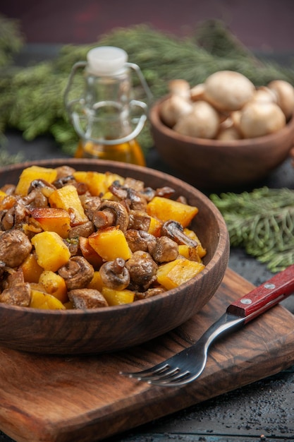 Seitenansicht Speiseöl und Zweige braune Schüssel Kartoffeln mit Pilzen auf dem Schneidebrett neben der Gabel unter Öl Schüssel mit weißen Champignons und Fichtenzweigen