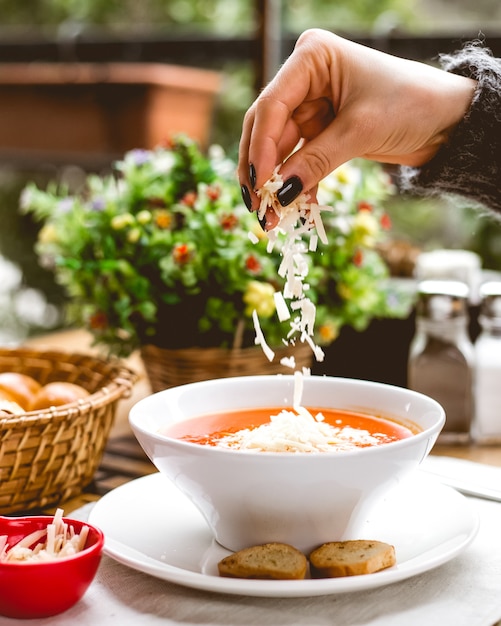 Seitenansicht streut eine Frau Tomatensuppe geriebenen Käse und Cracker