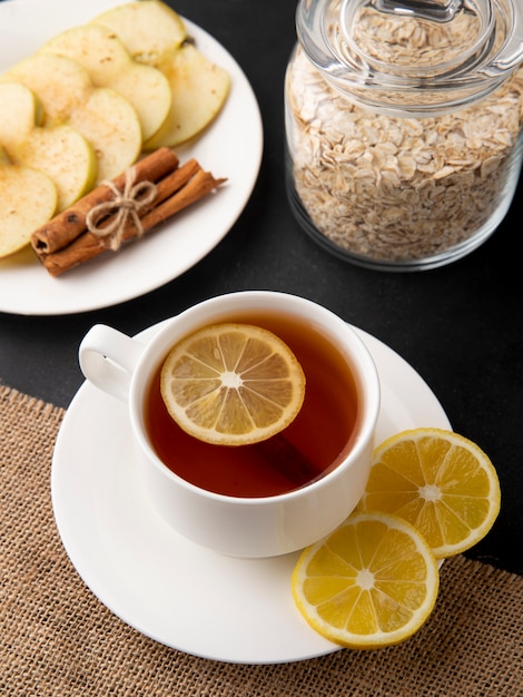 Seitenansicht Tasse Tee mit Zitronenscheiben und Apfelscheiben mit Zimt auf einem Teller