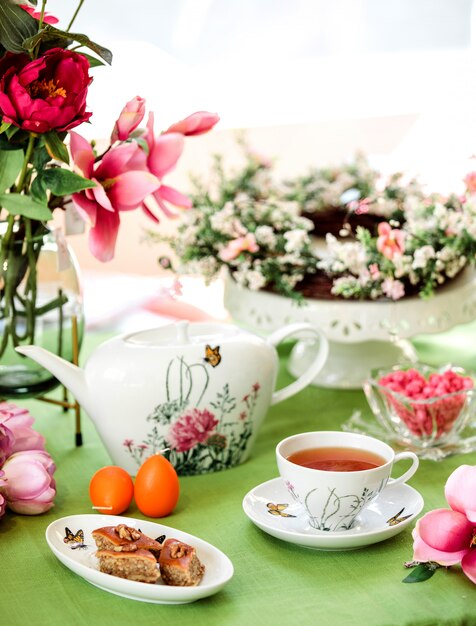 Seitenansicht traditionelles aserbaidschanisches süßes Baklava mit einer Tasse Tee mit einer Teekanne und Blumen auf dem Tisch