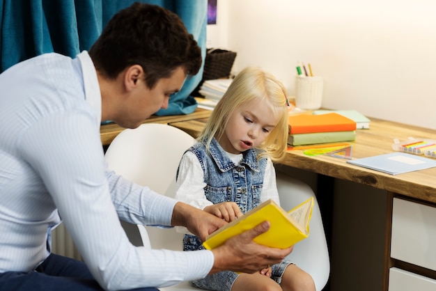 Kostenloses Foto seitenansicht vater hilft mädchen beim lesen