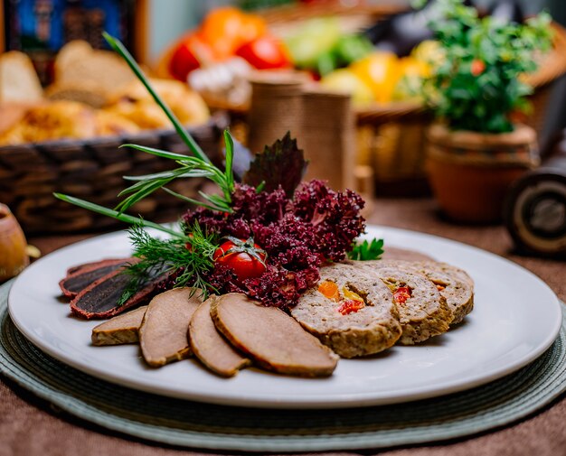 Seitenansicht verschiedene Fleischplatte kalt gekochtes Schweinefleisch Roulade Basdirma Tomate und Gemüse auf einem Teller