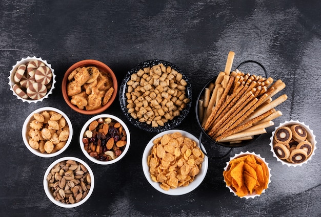 Kostenloses Foto seitenansicht verschiedener arten von snacks als nüsse, cracker und kekse in schalen mit kopierraum auf dunkler oberfläche horizontal