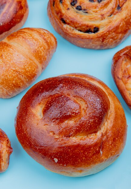 Seitenansicht verschiedener Backwaren als Croissant Brioche Pain aux Rosinen auf blauer Oberfläche