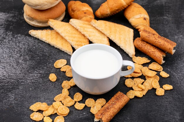 Seitenansicht verschiedener Brotsorten als Cracker, Toast, Croissants und Milch auf schwarzer Fläche horizontal