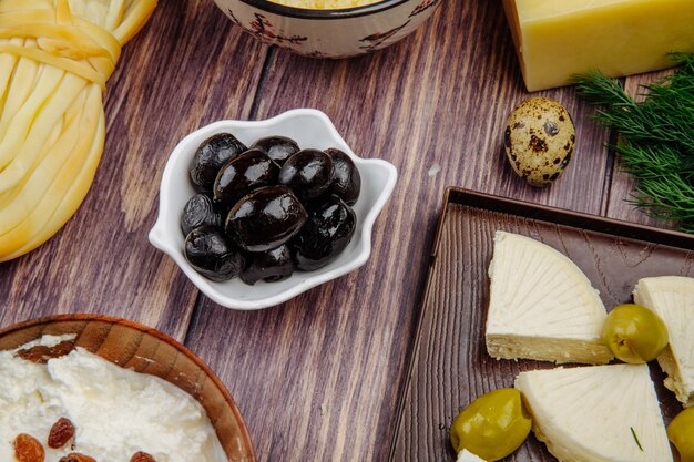 Seitenansicht verschiedener Käsesorten mit schwarzen eingelegten Oliven und Wachteleiern auf rustikalem Holz