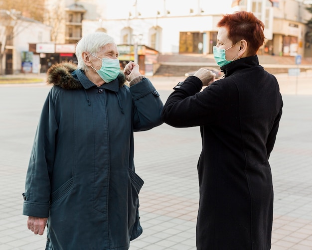 Seitenansicht von älteren Frauen mit medizinischer Maske, die Ellbogen berührt, um sich gegenseitig zu grüßen