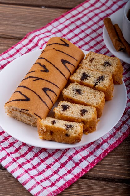 Seitenansicht von Biskuitkuchen mit Schokolade auf einem weißen Teller, der mit einer Tasse Tee serviert wird