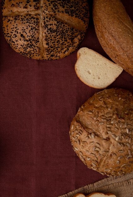 Seitenansicht von Broten als gesäte Cob-Weißbrotscheibe und Bagel auf burgunderfarbenem Hintergrund mit Kopienraum