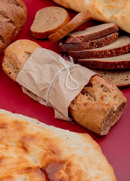 Seitenansicht von Broten als knuspriges Baguette-Tandir-Schwarz-Roggenbrot in Scheiben auf Bordo-Oberfläche