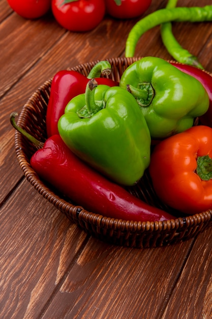 Seitenansicht von buntem Paprika des frischen Gemüses rote Chilischoten in einem Weidenkorb auf rustikalem Holztisch