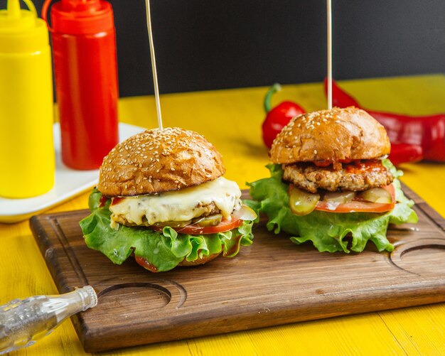 Seitenansicht von Burgern mit geschmolzenem Hähnchenschnitzelkäse und von Tomaten auf Holzbrett