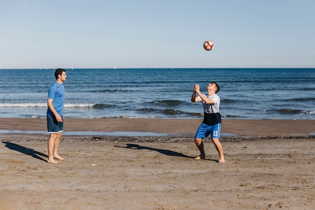 Kostenloses Foto seitenansicht von den freunden, die fußball am strand spielen