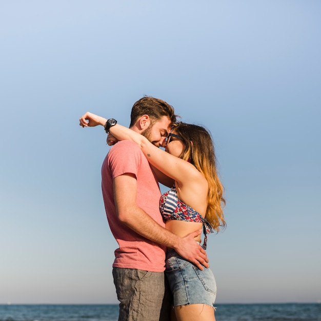 Seitenansicht von den romantischen jungen Paaren, die gegen blauen Himmel am Strand stehen