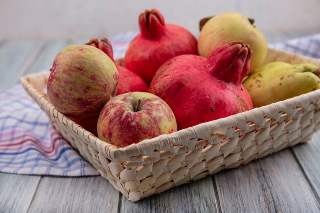 Seitenansicht von frischen Früchten wie Granatapfeläpfeln und Quitten auf einem Eimer auf einem karierten Tuch auf einem grauen Hintergrund