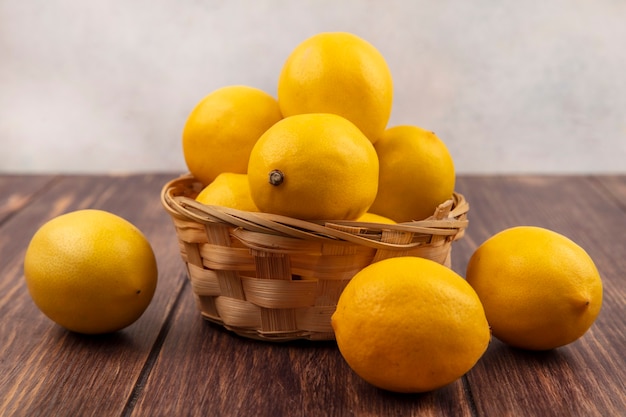 Seitenansicht von frischen gelbhäutigen Zitronen auf einem Eimer mit Zitronen lokalisiert auf einem Holztisch auf einer weißen weißen Wand