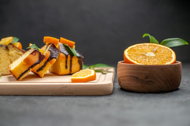 Seitenansicht von frischen Orangenscheiben und frisch gebackenen gehackten Kuchenscheiben auf dunklem Tisch