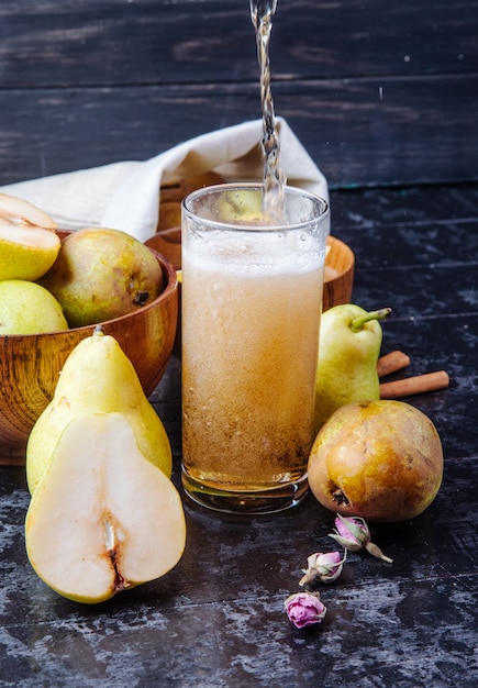 Seitenansicht von frischen reifen Birnen und Birnenhälften mit einem Glas Limonade auf schwarzem hölzernem Hintergrund