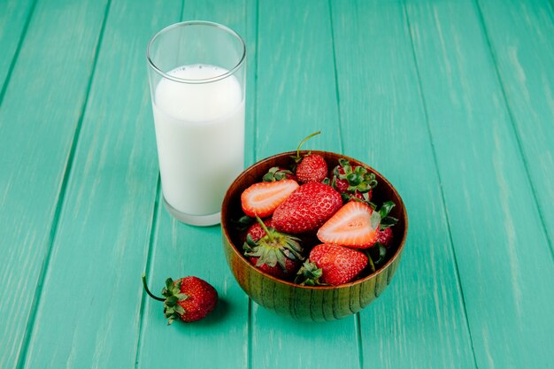 Seitenansicht von frischen reifen Erdbeeren in einer Holzschale mit einem Glas Milch auf grünem Holz