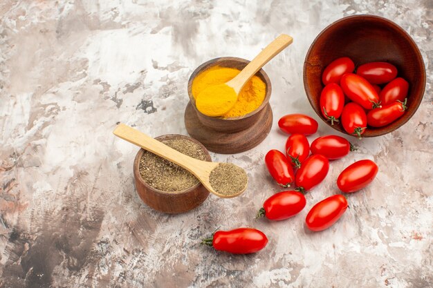 Seitenansicht von frischen Tomaten, die aus einem kleinen Topf und verschiedenen Gewürzen auf grauem Hintergrund gefallen sind