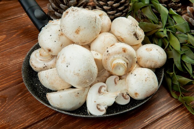 Seitenansicht von frischen weißen Pilzen auf einer Pfanne auf Holzoberfläche