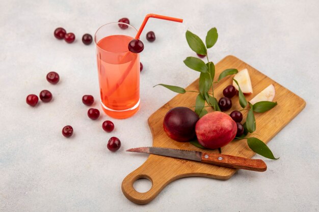 Seitenansicht von Früchten als Pfirsich und Kirsche mit Messer auf Schneidebrett und Kirschsaft auf weißem Hintergrund