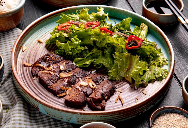 Seitenansicht von gebratenem Rindfleisch mit Salat und rotem Chili auf einem Teller auf Holz